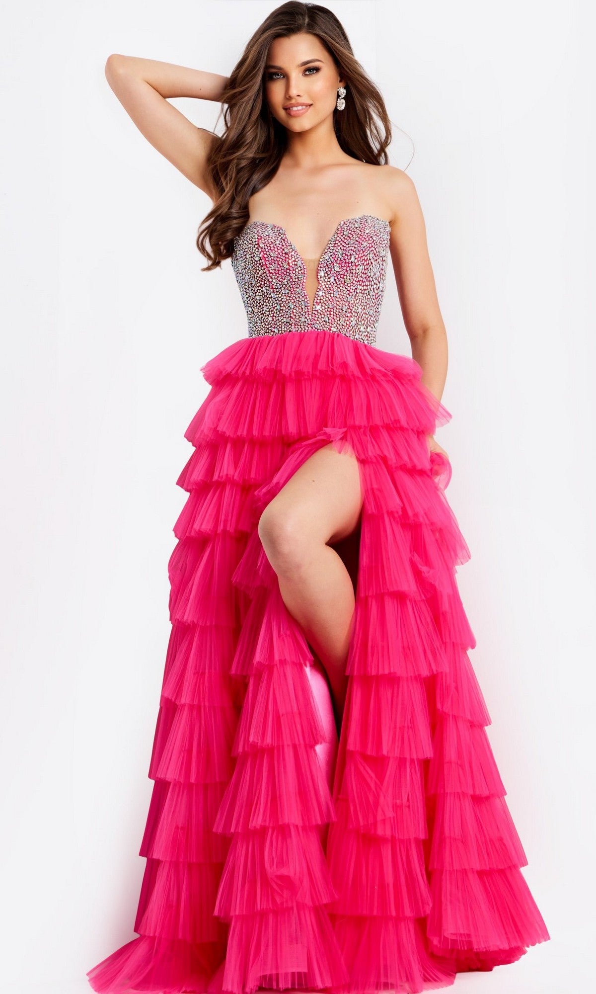 A woman models the Jovani 44360 long prom dress in fuchsia, featuring a strapless beaded bodice, rhinestone-embellished corset, multiple layers of bright pink ruffles, and a high slit, against a plain white background.